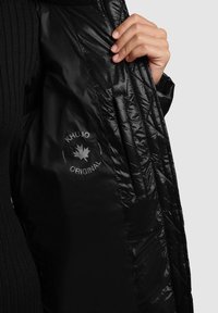 Czarna kurtka puchowa o błyszczącej powierzchni, z logo wewnątrz. Podszewka o fakturze z pikowanym wzorem dla ocieplenia.