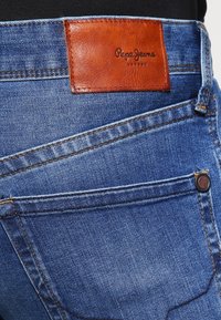 Närbild av blå denimjeans bakficka med brunt lädermärke från Pepe Jeans London.