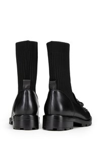 Botas negras hasta el tobillo con parte superior de punto texturizado y tacón de cuero liso. Presentan una pestaña para tirar y suela de goma gruesa con un dibujo estampado.
