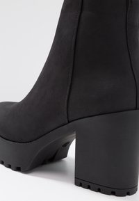 Stivaletto nero con tomaia testurizzata, tacco a blocco robusto e suola spessa. Presenta cuciture laterali e una finitura liscia.