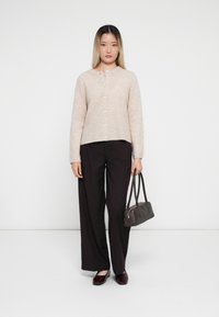 Ljusbeige button-up cardigan med rund halsringning, kombinerad med mörka ränder i vida byxor och en liten mörk handväska. Skorna är burgundy.