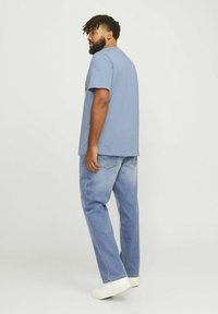 Camiseta de algodón azul claro con mangas cortas y escote redondeado, combinada con jeans azul claro de pierna recta y zapatillas blancas.