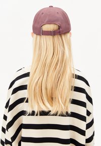 Lila Baseballcap von hinten betrachtet, mit einem verstellbaren Riemen. Getragen mit einem übergroßen Oberteil in Schwarz-Weiß gestreift. Glatte Textur.