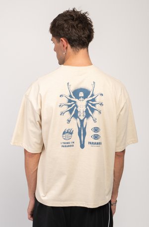 Cream-colored oversized t-shirt made of cotton; features a blue graphic print on the back depicting a figure surrounded by symbols.