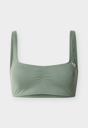 Zachtgroene cropped sportbeha met brede bandjes en subtiel gerimpeld middenstuk, met een klein wit logo aan de linkerkant.