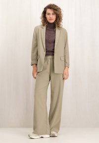 Lichtgroene, op maat gemaakte blazer met een enkele knoop en zakken, gecombineerd met bijpassende wijde broek en een donker gestructureerd coltruitje.