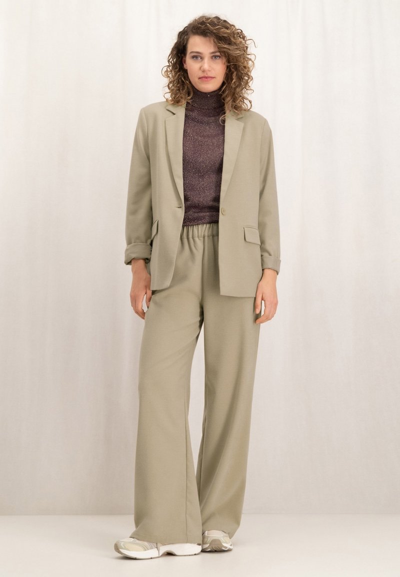Lichtgroene, op maat gemaakte blazer met een enkele knoop en zakken, gecombineerd met bijpassende wijde broek en een donker gestructureerd coltruitje.