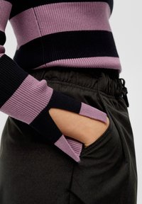 Sweter w prążki z dzianiny w kolorze czarnym i liliowym z wycięciem przy nadgarstku, zestawiony z czarnymi spodniami na elastycznym pasie.