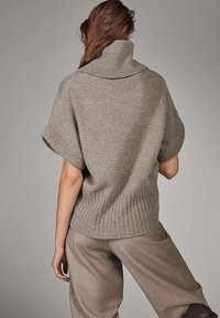 Lyhythihainen harmaa neulepusero, jossa on korkea, resorinen kaulus. Pehmeä, neulottu rakenne ja rento istuvuus. Yhdistetty vaaleanharmaisiin housuihin yhtenäisen ilmeen luomiseksi.