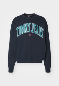 Sudadera azul marino de algodón, con texto en blanco y azul claro "TOMMY JEANS". Mangas y dobladillo acanalados, con un pequeño logotipo de bandera.
