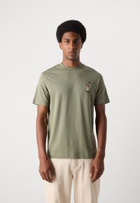 Olijf groene katoenen T-shirt met een ronde hals en korte mouwen, voorzien van een klein geborduurd ontwerp op de linkerkant van de borst.