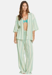 Kevytrakenteinen, raidallinen pyjama-asusetti mintunvihreänä ja kermanvärisenä. Sisältää löysän nappipuseron ja leveälahkeiset housut, joissa on joustava vyötärö.