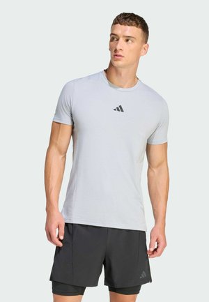 Light gray athletic t-shirt with a crew neck and short sleeves, featuring a small black Adidas logo on the chest, paired with black shorts.
