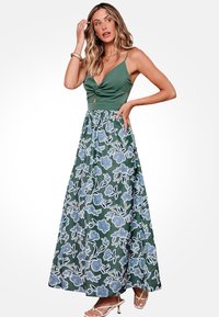 Vestido maxi con un top verde ajustado que presenta un detalle retorcido, y una falda floral fluida en azul y blanco con un patrón de hojas.