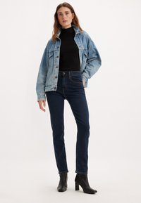 Giacca di jeans azzurra con vestibilità rilassata, abbinata a jeans scuri a vita alta. Stivali neri con tacco alto completano l'outfit.