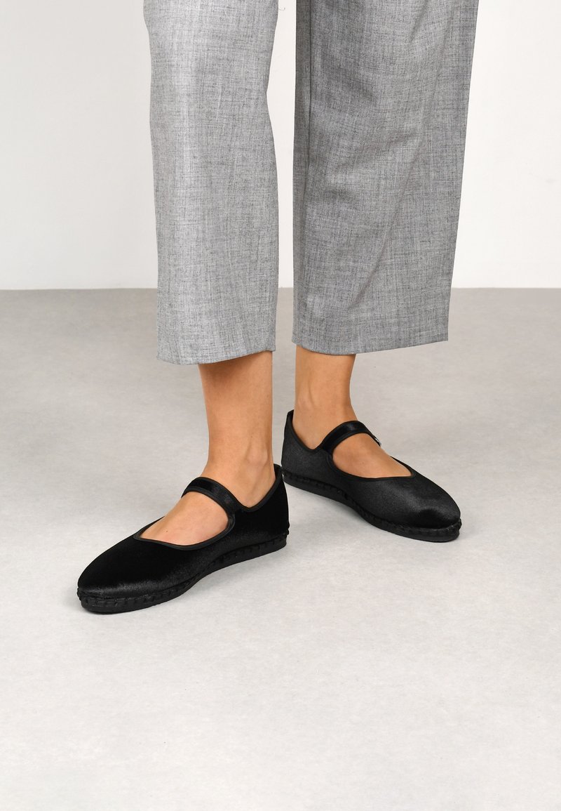 Zapatos Mary Jane negros, hechos de material suave, con suela plana, punta redonda y una correa a través del empeine. Acabado en tela texturizada.