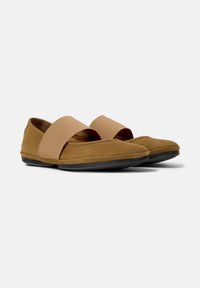 Zapatos marrones sin cordones con una banda elástica ancha, que presentan un diseño elegante y una suela plana de goma, sobre un fondo blanco liso.