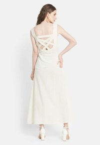 White midi dress with a textured fabric, wide straps, and a crisscross open back design. Paired with white block-heel shoes.