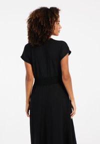 Robe noire, longueur cheville avec manches courtes, détail de taille froncée et tissu texturé. Design simple et fluide sans motifs.