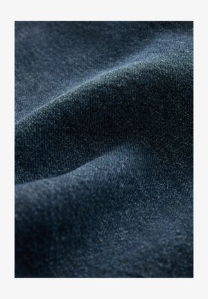 Temno modra denim tkanina z gladko teksturo, poudarjena z diskretnimi variacijami v tkanju. Ima mehko sijaj in rahlo elastičnost.