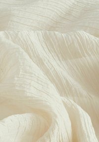 Tissu crème texturé avec un motif froncé, présentant une apparence légère et aérée, idéal pour diverses applications textiles.
