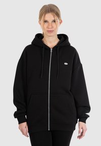 Felpa nera con zip realizzata in tessuto morbido. Caratterizzata da un ampio cappuccio, tasche frontali e un logo ricamato sul petto. Vestibilità larga e comoda.