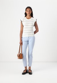 Bílý pletený top s krátkým rukávem a černým lemem, kombinovaný se světle modrými slim-fit kalhotami. Doplňky zahrnují hnědou crossbody tašku a černé boty.