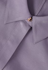 Fialový košeľový golier z látky so zapínaním na jeden lesklý gombík v ružovozlatej farbe, ktorý spája konce goliera.