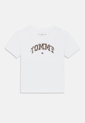 T-shirt blanc à manches courtes avec "TOMMY" en lettrage imprimé léopard. Il présente un col rond et un détail de bouton sur une épaule. Tissu en coton lisse.