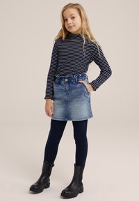 Črtasta dolgosleča turtleneck majica, denim A-linija krilo, temni leggingi in črne gležnjarje; sproščen videz z raznolikimi teksturami in barvami.