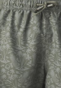 Bañador verde claro con un patrón de piñas y palmeras. Presenta una cintura elástica con cordón y una textura suave.