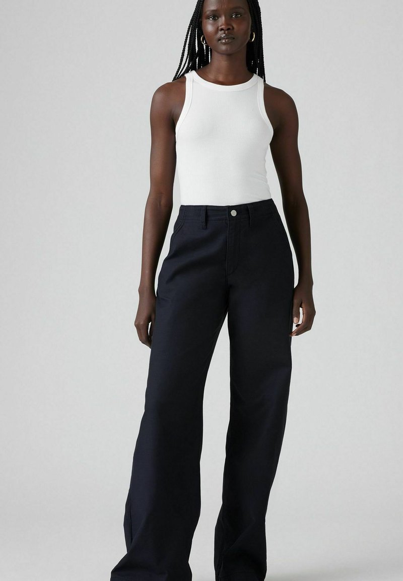 Top bianco a coste abbinato a pantaloni larghi blu navy. I pantaloni presentano una chiusura con bottone e cuciture in contrasto. Tessuto dalla trama liscia.