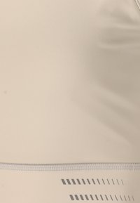 Beige urheilusarja, joka on valmistettu sileästä materiaalista, jossa on leveä nauha, jossa on hillitty painettu kuvio vaakasuorista viivoista ja geometrisista muodoista.