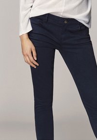 Marineblauwe stretchbroek met een slim fit, voorzien van voorzakken en een knoopsluiting. Het materiaal lijkt zacht en glad van structuur.