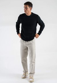 Maglione a maglia scura con scollatura rotonda, pantaloni cargo beige chiaro e sneakers beige con dettagli bianchi, indossati da un uomo in piedi.