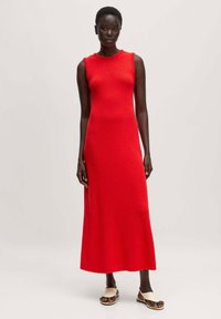 Rotes ärmelloses Strick-Maxikleid mit strukturiertem Muster, rundem Ausschnitt und gerader Silhouette, kombiniert mit hellen flachen Sandalen.
