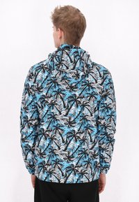 Jachetă cu glugă, cu un imprimeu vibrant de frunze de palmier în nuanțe de albastru, negru și alb. Fabricată din material ușor, cu manșete și tiv elastic.