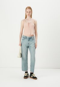 Haut court rose clair avec des boutons, jeans taille haute bleu clair, baskets noires et crème, et un petit sac à bandoulière blanc.