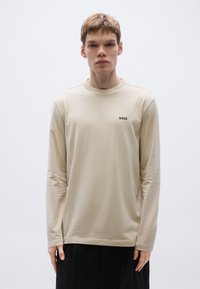 Hosszú ujjú bézs póló kerek nyakkivágással és egy kis fekete "BOSS" logóval a mellrészen. Puha anyagú, laza szabású.