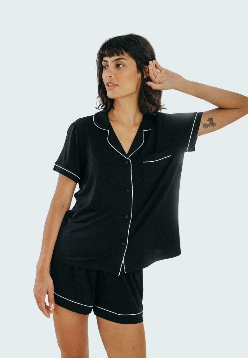 Czarny zestaw piżamowy wykonany z miękkiego materiału, z krótkim rękawem zapinanym na guziki, wykończony białymi lamówkami oraz dopasowanymi szortami o luźnym kroju.