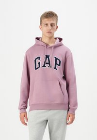 Pullover hoodie in light purple, featuring a large navy "GAP" logo. Made of cotton blend, with a front pocket and adjustable drawstring hood.
