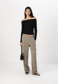 Černý off-the-shoulder top s dlouhým rukávem v kombinaci s béžovými širokými kalhotami. Doplňky zahrnují malou černou tašku a vzorované slip-on boty.