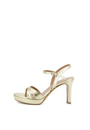 Sandalo dorato con tacco alto, cinturino alla caviglia, punta aperta e leggera zeppa, mostrato su sfondo bianco.
