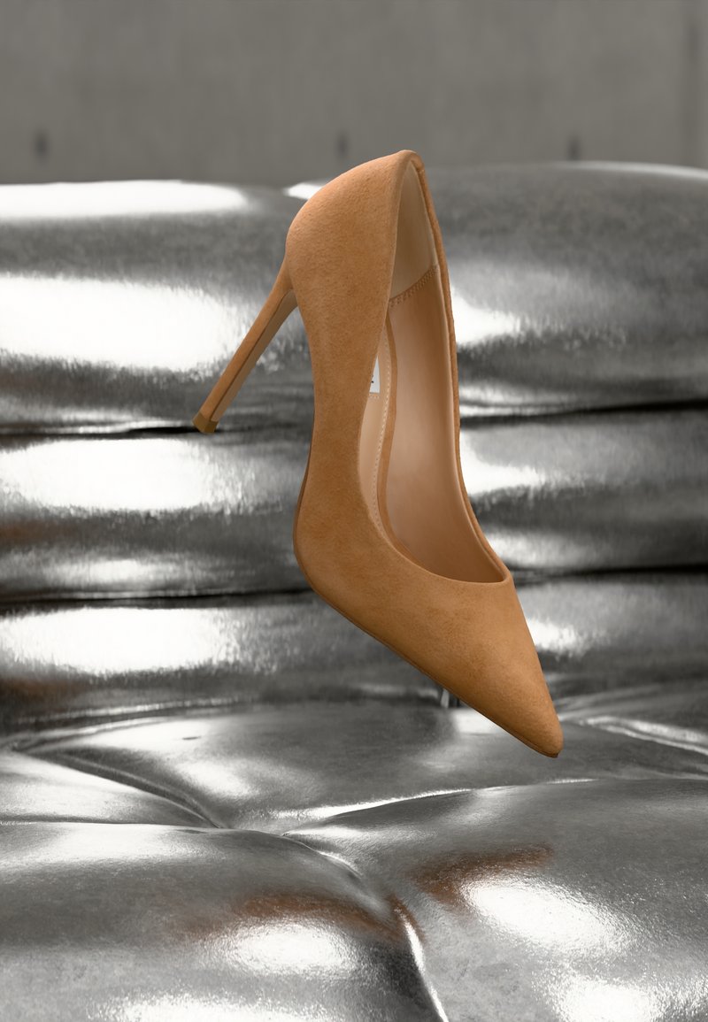 Καστόρινο τακούνι σε απόχρωση ταμπά που αιωρείται πάνω από μια γυαλιστερή ασημένια επιφάνεια από δέρμα με καπιτονέ, γωνιασμένο για να δείχνει το πλευρό και την εσωτερική σόλα.