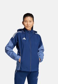 Marineblauer Windbreaker mit Kapuze, elastischen Bündchen und hellblauen Akzenten. Hergestellt aus leichtem, wasserabweisendem Material.