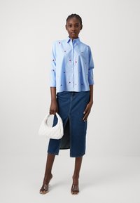 Lichtblauw gestreept button-up shirt met rode hartversieringen, gecombineerd met een hooghangende spijkerrok en een witte gewatteerde handtas.