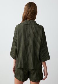 Olivengrünes Zweiteiler-Set bestehend aus einem locker sitzenden gestreiften Kurzarmoberteil und passenden Shorts, das ein strukturiertes Stoffdesign zeigt.