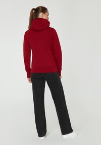 Sudadera roja con una gran capucha y puños acanalados, combinada con pantalones negros de pierna recta y zapatillas blancas. Diseño simple y casual.