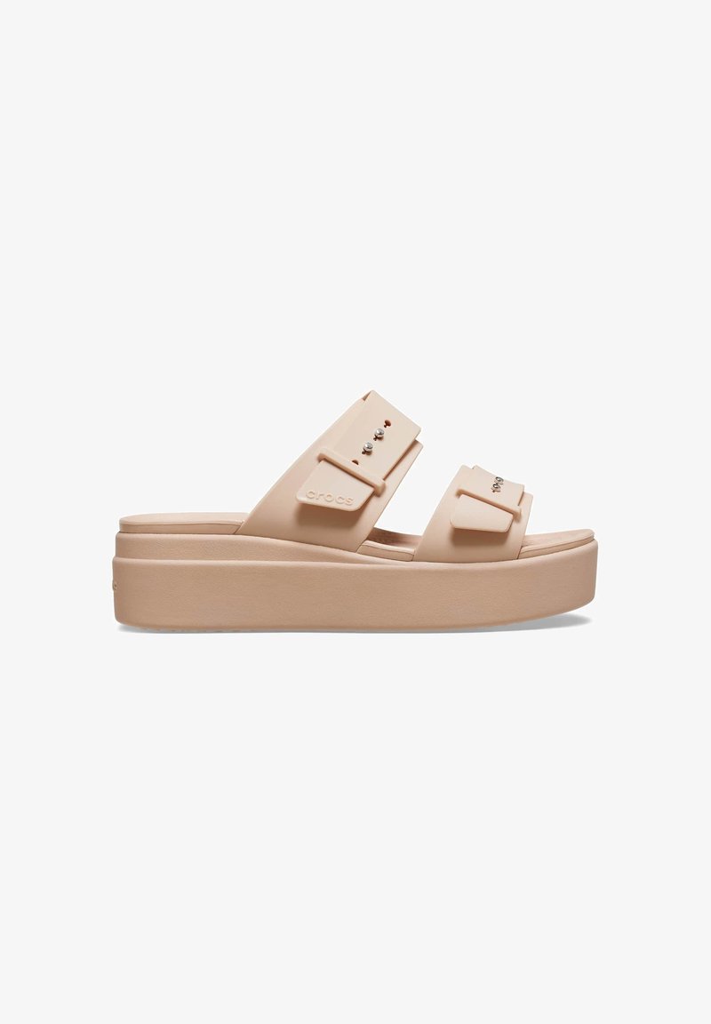 Helle beige Plattform-Sandalen mit zwei breiten Riemen, die mit dekorativen Nieten versehen sind. Sie bestehen aus strapazierfähigem Material und haben eine glatte, strukturierte Sohle.