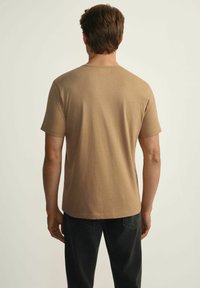 Brązowa koszulka z krótkim rękawem z bawełny, z chropowatym, nakrapianym wzorem. Koszulka ma okrągły dekolt i luźny krój.